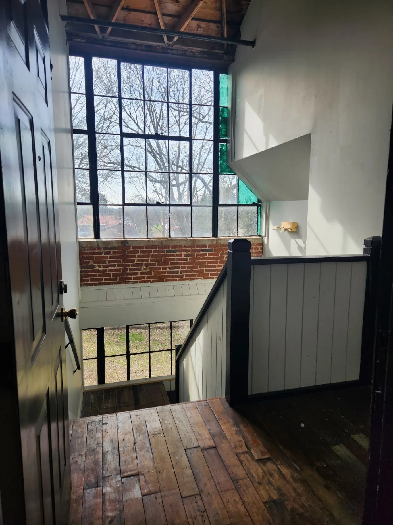 Interior landing with a tall window, brick wall, and stair railing